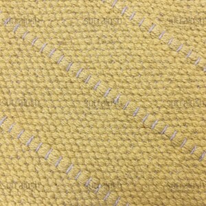 May include: Close-up of a textured yellow fabric with diagonal rows of white stitching. The fabric has a woven appearance with a slightly raised, dotted texture. The stitching is evenly spaced.