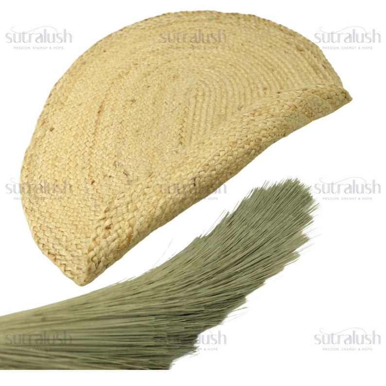 May include: A half-circle, woven jute rug in a natural beige color. The rug has a textured surface and a braided edge. A bundle of light green fibers is in the foreground, possibly a brush or decorative element.