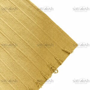May include: Mustard yellow woven rug with vertical ribbed pattern and fringe detail. The rug's texture is visible, and the corner is shown against a white background. The rug is a home decor item.