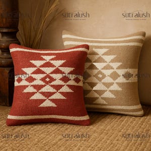 May include: Two decorative throw pillows with geometric patterns. One pillow is a deep red with a white diamond and triangle design. The other is tan with a similar white pattern. The pillows are on a woven surface.