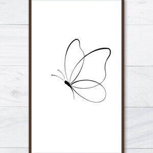 K&ouml;nnte beinhalten: Gerahmter Druck mit einer minimalistischen schwarzen Strichzeichnung eines Schmetterlings auf wei&szlig;em Hintergrund. Der Schmetterling ist mit einfachen, eleganten Linien dargestellt. Der Rahmen ist dunkelbraun und bildet einen Kontrast zum Kunstwerk.