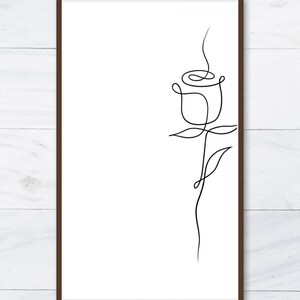 K&ouml;nnte beinhalten: Ein gerahmter Druck mit einer minimalistischen Strichzeichnung einer Rose. Der schwarze Umriss der Blume ist vor einem wei&szlig;en Hintergrund mit einem braunen Rahmen abgebildet. Das Kunstwerk zeigt eine einzelne Rose mit Stiel und Bl&auml;ttern.