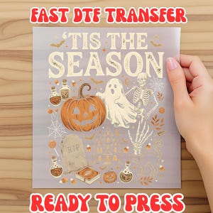 May include: A rectangular DTF transfer sheet featuring the text 'TIS THE SEASON' in a cream font. The design includes a large orange pumpkin, a white ghost, a skeleton, a tombstone marked 'RIP', potion bottles, a haunted house, and candy corn.