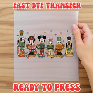 May include: A clear sheet featuring a colorful design of Disney characters dressed as nutcrackers. The characters include Mickey Mouse, Minnie Mouse, Donald Duck, Daisy Duck, Goofy, and Pluto. Text at the top reads "FAST DTF TRANSFER" and at the bottom "READY TO PRESS".