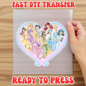 May include: A heat transfer sheet featuring a heart-shaped design with cartoon princesses in various colorful gowns. The text "FAST DTF TRANSFER" and "READY TO PRESS" are in red, outlined in white.