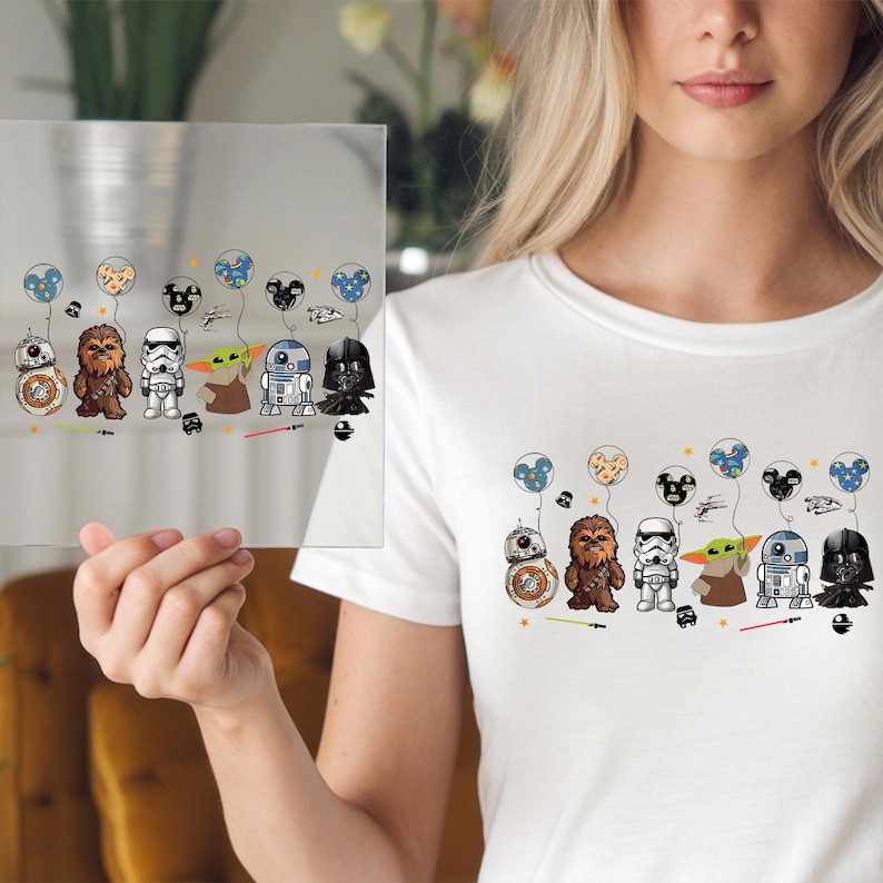 May include: White t-shirt featuring a colorful graphic of Star Wars characters holding balloon bouquets. The characters include BB-8, Chewbacca, a Stormtrooper, Yoda, R2-D2, and Darth Vader. The design is repeated on a clear glass panel.