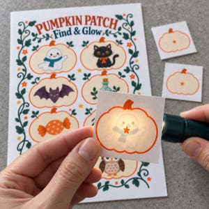 May include: A Pumpkin Patch Find & Glow activity sheet featuring illustrated pumpkins with a ghost, cat, bat, potion, candy, and owl. A small square card with a ghost pumpkin is illuminated by a flashlight, revealing a hidden star.