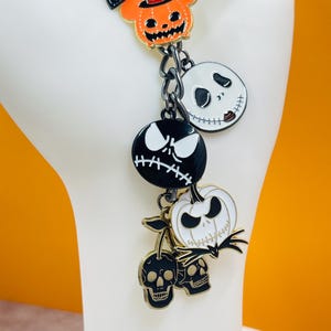 Puede incluir: Una pulsera de dijes con colgantes tem&aacute;ticos de Halloween. Los dijes incluyen a Jack Skellington, una calabaza con sombrero de copa y dise&ntilde;os de calaveras. Los dijes son negros, blancos y naranjas con detalles dorados, unidos por una cadena de metal oscuro.