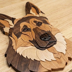 May include: Wooden wall art depicting a German Shepherd dog's head, constructed from different wood tones. The artwork showcases detailed eyes, nose, and fur patterns, using a natural palette of browns and tans. The piece is mounted on a wooden surface.