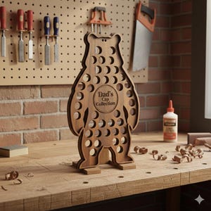 May include: A wooden bear-shaped cap organiser with numerous circular holes. The text "Dad's Cap Collection" is engraved in a circle on the bear's chest. The organiser is made of light brown wood and stands on a wooden surface.