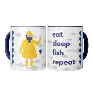 Peut inclure: Mug en céramique blanche avec une anse et un bord bleu marine. Un côté présente un pêcheur de dessin animé en manteau jaune, l'autre côté porte l'inscription "eat sleep fish repeat" en bleu marine. Des illustrations de poissons sont dispersées.