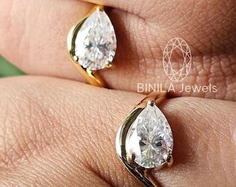 May include: Two gold rings with pear-shaped, clear gemstones are displayed. The rings have a unique, curved design. The brand name "BINILA Jewels" is visible in the image. The rings are on a person's fingers.