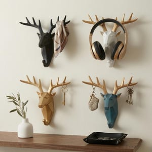 Puede incluir: Conjunto de colgadores de pared decorativos con forma de cabeza de ciervo. Los colgadores son de varios colores, incluyendo negro, dorado, blanco y azul. Algunos colgadores sostienen objetos como auriculares, llaves y bufandas. Las cornamentas son doradas.
