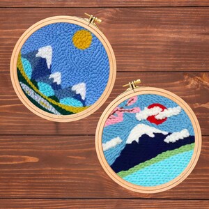 以下が含まれることがあります： 山岳風景のデザインが施された2つの丸い刺繍枠。1つは黄色い太陽、雪をかぶった山、青い空が特徴です。もう1つは赤い太陽、ピンクの花、雪をかぶった山があります。