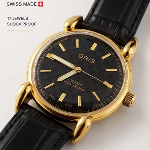May include: An Oris wristwatch with a gold-tone round case and a black textured dial. The watch features gold-tone hour markers, luminous hands, and the text ORIS, 7 JEWELS, and SHOCK PROOF on the face. It has a black leather strap with a crocodile pattern.