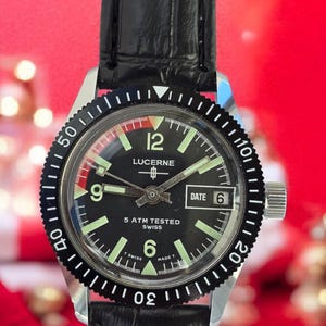 May include: A vintage Lucerne watch with a black dial, luminous hands and markers, and a date window at the 3 o'clock position. The watch has a black bezel with white markings, a stainless steel case, and a black leather strap. The watch reads "5 ATM TESTED SWISS".