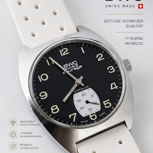 May include: A BWC Swiss Courage wristwatch with a black dial, white Arabic numerals, and a white perforated rubber strap. The watch features a sub-dial for seconds, silver hands, and text including BWC, Swiss Made, and Incabloc on the face.