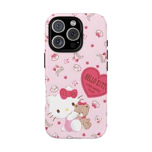 May include: Pink phone case featuring Hello Kitty and a teddy bear. The case has a repeating pattern of hearts, bows, and floral elements. A heart-shaped graphic reads "Hello Kitty: A little something for you."