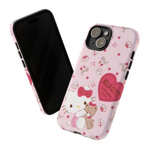May include: Pink phone case featuring Hello Kitty with a teddy bear, surrounded by hearts, bows, and other small illustrations. The case also has the text "Hello Kitty: A little something for you."