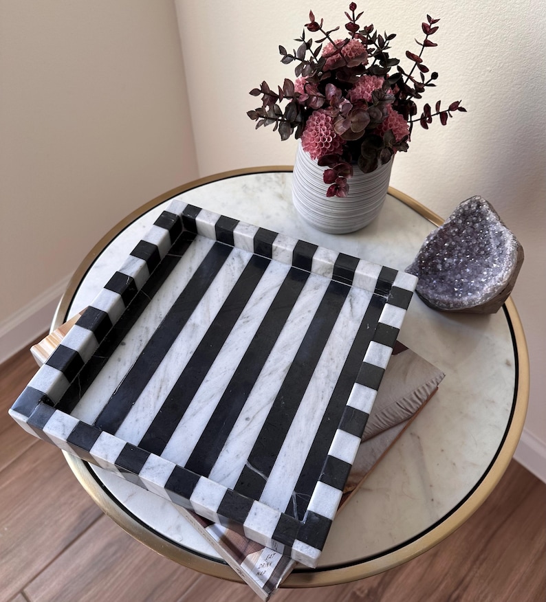 May include: A square tray featuring a bold black and white striped pattern. The tray has raised edges with a matching alternating black and white block design. The surface of the tray is smooth and flat, showcasing a high-contrast geometric aesthetic.