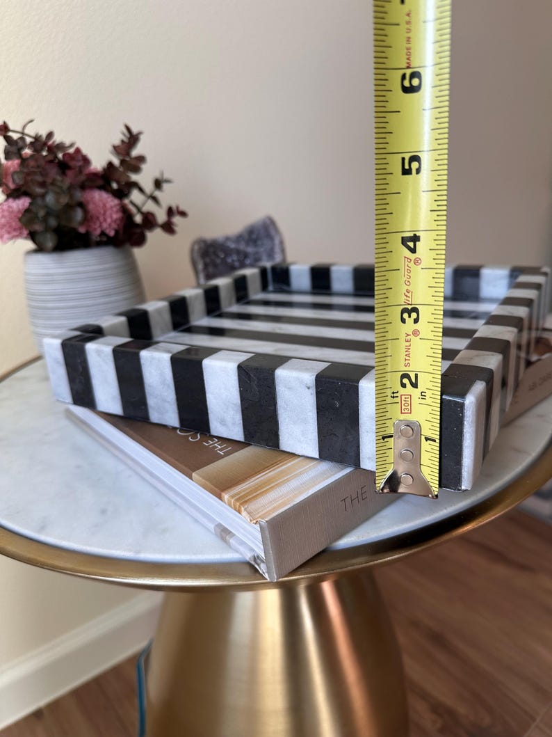 May include: A rectangular tray featuring a bold black and white striped pattern made of stone. A yellow Stanley measuring tape is positioned vertically against the side of the tray, indicating a height of approximately 2.5 inches for the rim.