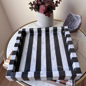 May include: A rectangular tray crafted from polished stone featuring a bold, high-contrast pattern of vertical black and white stripes. The tray has raised edges with a matching striped design that continues along the perimeter of the frame.