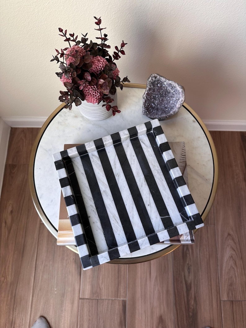 May include: A square tray featuring a bold pattern of alternating black and white vertical stripes. The tray has raised edges and a smooth, polished surface, showcasing a distinct contrast between the dark and light color bands throughout.