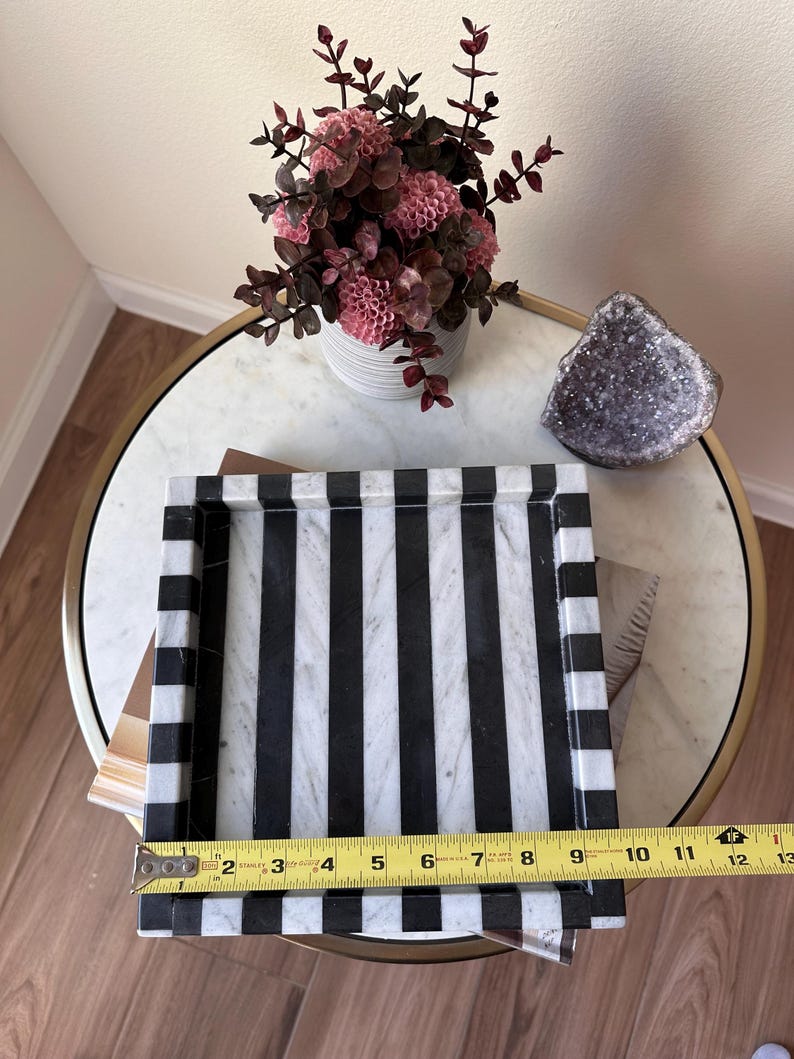 May include: A rectangular tray featuring alternating black and white marble stripes. A yellow Stanley measuring tape is placed across the front edge, indicating a width of approximately 12 inches. The tray has raised edges and a smooth, polished finish.
