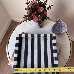 May include: A rectangular marble tray featuring a bold black and white vertical striped pattern. A yellow Stanley measuring tape is positioned across the front edge, indicating a width of approximately 11.5 inches for the tray's interior base.