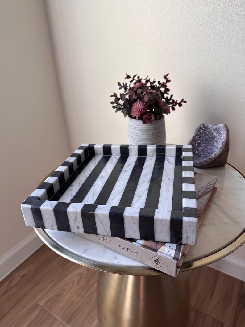 May include: A square tray featuring a bold black and white striped pattern. The tray is constructed with thick, raised edges and a flat base, showcasing a smooth, polished stone-like texture with alternating dark and light vertical stripes.