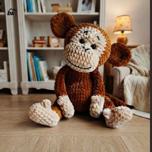 Puede incluir: Un peluche de mono hecho de hilo marrón y crema con un patrón de puntadas texturizadas y en bucle. El mono presenta orejas grandes y redondas, una boca ancha sonriente y ojos de plástico oscuro, sentado con las extremidades extendidas.
