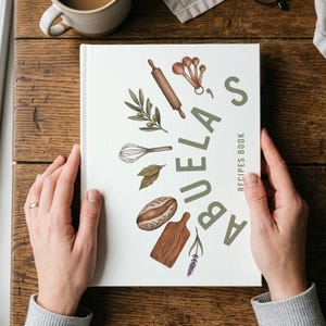 Puede incluir: Un libro de cocina blanco titulado "Abuela's Recipes Book" está abierto. La portada presenta ilustraciones de utensilios de cocina e ingredientes, incluyendo un rodillo, cucharas medidoras y pan. El título es verde, con la palabra "Recipes Book" en letra más pequeña.