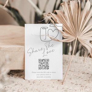 May include: A white card with the words "Share The Love" and a QR code. The card features a line drawing of a camera with a heart. The text "Please scan the QR code to share your photos with us RACHEL & JOHN" is also present.