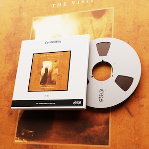 Könnte beinhalten: Ein weißes Albumcover mit dem Text "OpenReelShop" und "Loreena McKennitt The Visit" in Schwarz. Das Albumcover hat ein gold-schwarzes Bild. Ein silbernes Tonband ist neben dem Albumcover. Der Hintergrund ist goldfarben.