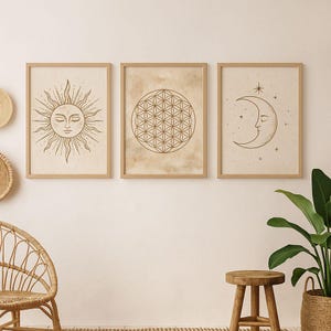 Peut inclure: Trois impressions d'art encadrées avec des motifs célestes. Les impressions présentent un soleil avec un visage, un motif de Fleur de Vie et un croissant de lune avec des étoiles. L'œuvre est dans des tons bruns et beiges, avec des cadres en bois.