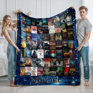 May include: A dark blue blanket featuring a collage of Stephen King book covers. The blanket has a starry background and the name "MICHAEL" at the bottom. The blanket is held by two people.