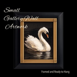 May include: A framed painting of a white swan on dark water. The frame is black with a gold inner border. Text on the image reads: Small Gallery Wall Artwork, Framed and Ready-to-Hang. The swan has a white body and an orange beak.