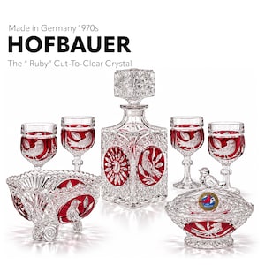 Puede incluir: Un juego de cristal Hofbauer Ruby tallado sobre vidrio transparente de los años 70, que incluye un decantador cuadrado con tapón, cuatro copas, un cuenco con base y un plato con tapa. Cada pieza presenta detalles en rojo con motivos de aves y flores.