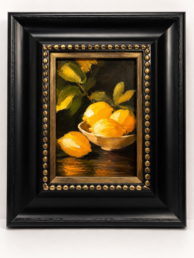 Puede incluir: Una pintura al &oacute;leo de limones de color amarillo brillante en un cuenco blanco sobre un fondo oscuro. La obra est&aacute; enmarcada en un marco negro grueso con un borde interior dorado que presenta una fila decorativa de peque&ntilde;os tachones met&aacute;licos.