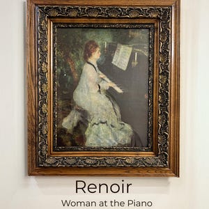 Puede incluir: Reproducción enmarcada de la pintura "Mujer en el piano" de Renoir. La obra presenta a una mujer con un vestido blanco tocando el piano, dentro de un marco de madera oscura y ornamentada. El texto "Renoir" y "Woman at the Piano" están debajo del marco.
