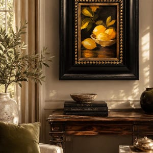 Puede incluir: Una pintura al &oacute;leo de limones amarillos en un cuenco, enmarcada en un marco de madera negra gruesa con adornos de tachuelas doradas. La obra muestra c&iacute;tricos brillantes sobre un fondo oscuro, montada en una pared sobre una mesa consola de madera.