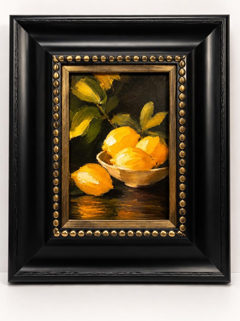 Puede incluir: Una pintura al &oacute;leo de limones de color amarillo brillante en un cuenco blanco sobre un fondo oscuro. La obra est&aacute; enmarcada en un marco negro grueso con un borde interior dorado que presenta una fila decorativa de peque&ntilde;os tachones met&aacute;licos.