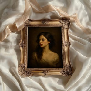 May include: A framed portrait of a woman with dark hair and a soft, neutral-toned dress. The ornate, gold-colored frame adds a vintage aesthetic. The artwork is set against a backdrop of draped, off-white fabric, with a ribbon accent.
