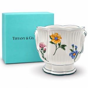 Peut inclure: Un cache-pot en céramique blanche avec un corps cannelé et un bord festonné, orné de motifs floraux peints en jaune, rose et bleu. Le cache-pot présente une bordure vert foncé et est placé à côté d'une boîte carrée Tiffany & Co. turquoise.