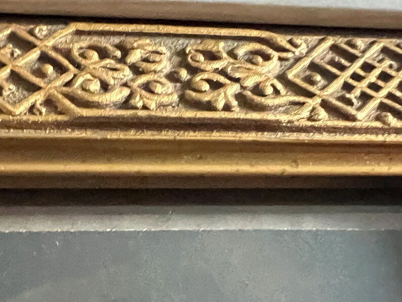 May include: Detail of a decorative gold frame with ornate patterns. The frame displays repeating floral and geometric designs, with a textured surface and a darker, aged finish. The frame is likely part of a larger artwork.