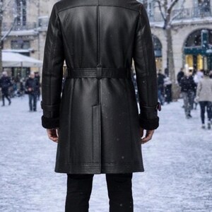 May include: A black leather coat with a black fur collar and a matching belt. The coat is worn over black pants and shoes. The background shows a snowy street scene with buildings and people.