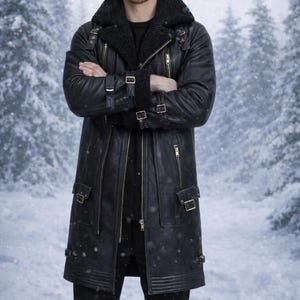 May include: A black leather coat with a shearling collar, multiple zippers, and buckle details. The long coat features a tailored fit and is worn over a black outfit. The background shows a snowy forest scene.