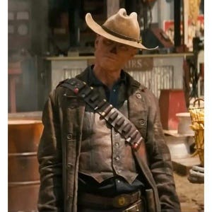 May include: A person wearing a brown leather duster coat, a cowboy hat, and a bandolier with bullets. The coat has multiple buttons and a dark brown color. The hat is tan with a curved brim. The bandolier is brown with red accents.