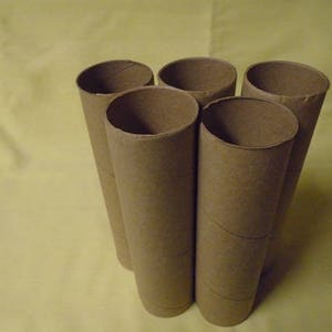 May include: Five brown cardboard tubes, possibly from paper towels or wrapping paper, are stacked in a pyramid shape on a yellow surface.