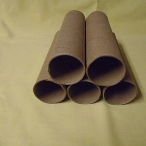 May include: Six brown cardboard tubes stacked in a pyramid shape. The tubes are empty and have a rough texture.